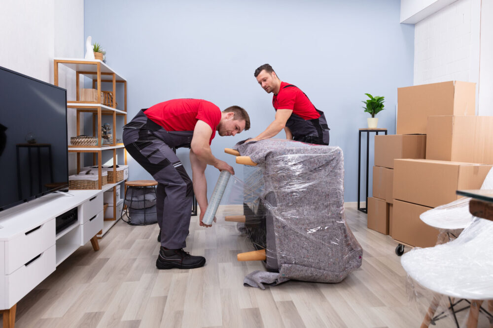 Movers wrapping a sofa in blankets and plastic wrap