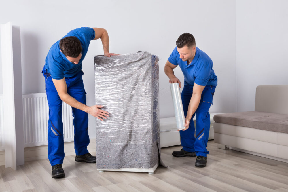 Cross-country movers wrapping furniture in a blanket and plastic wrap